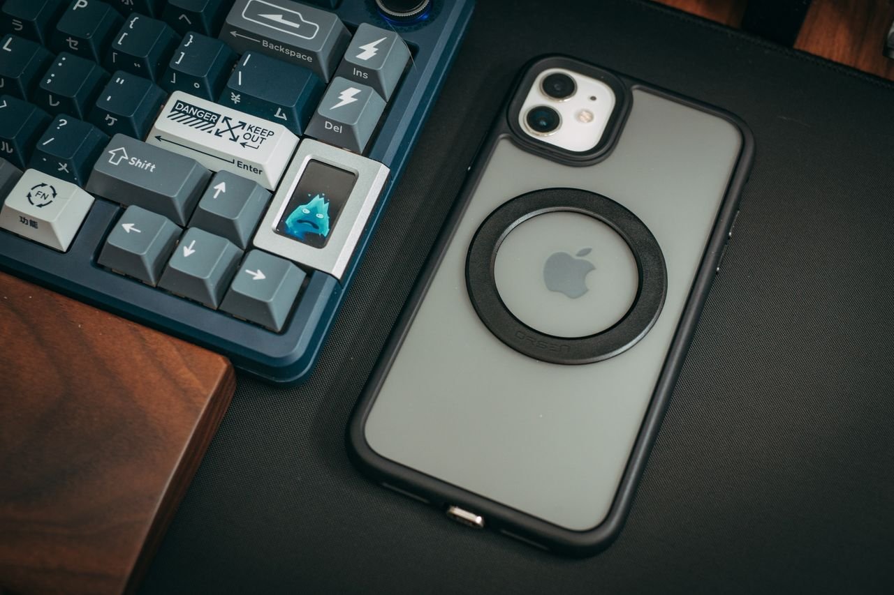 A close-up of a custom keyboard with keycaps and a smartphone on a sleek desk setup.